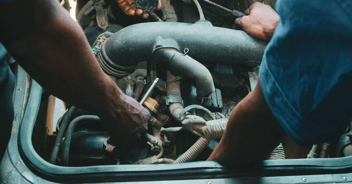 Des mécaniciens automobiles réparant un moteur dans un atelier nigérian. Gros plan sur les mains et les outils.