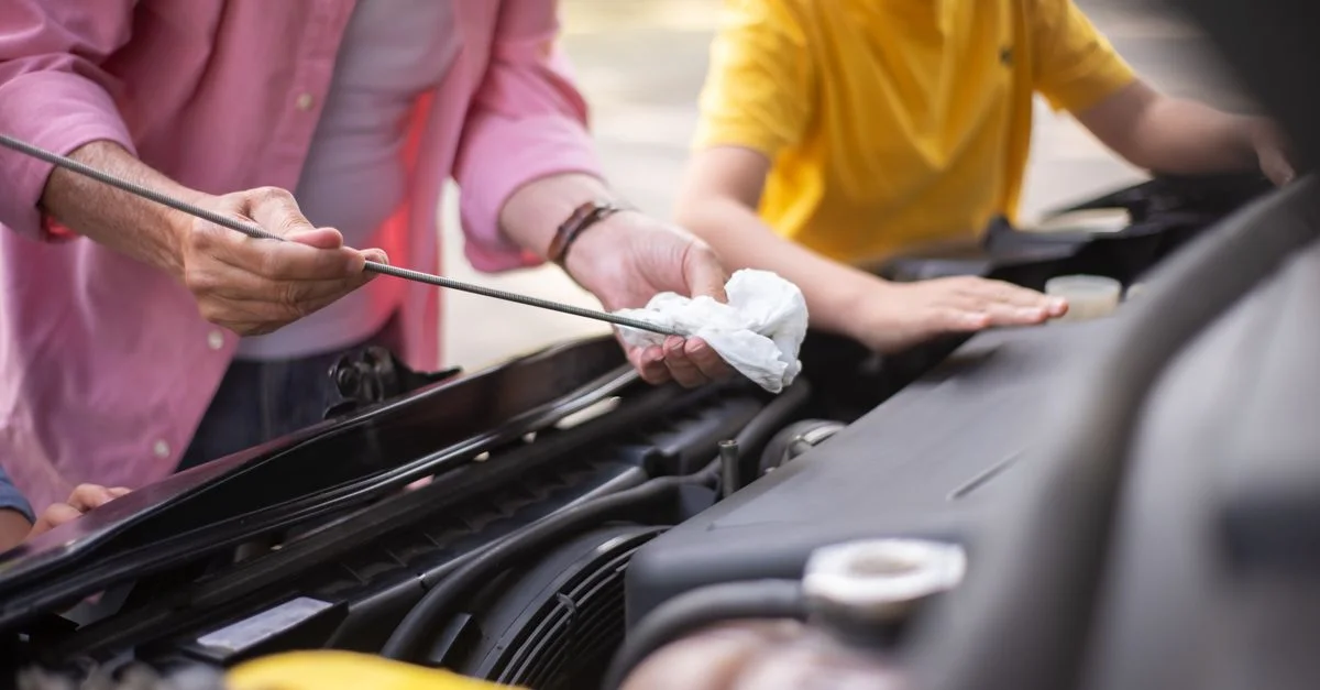 Père et fils travaillant sur l'entretien de la voiture, vérifiant l'huile du moteur en plein air.
