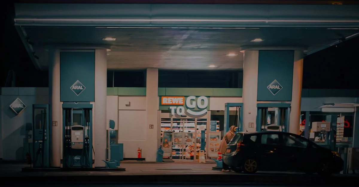 Une vue nocturne d'une station-service et d'un magasin de proximité avec une voiture garée à la pompe.
