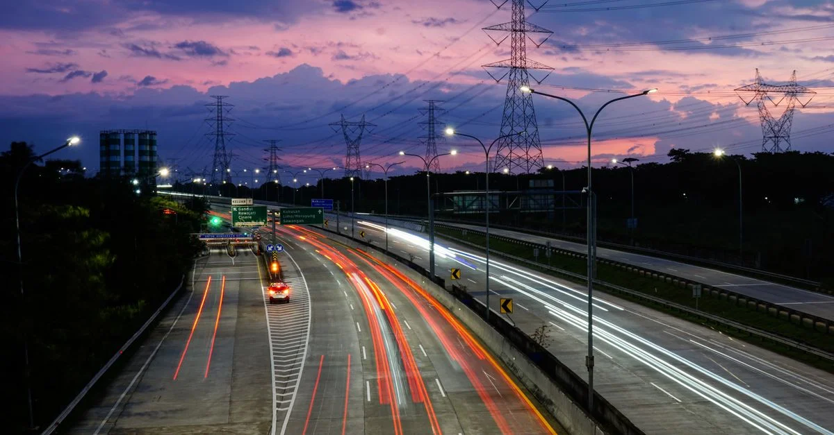 Traînées lumineuses vibrantes sur la route de péage de Jakarta au crépuscule, mettant en valeur le mouvement urbain et un ciel coloré.