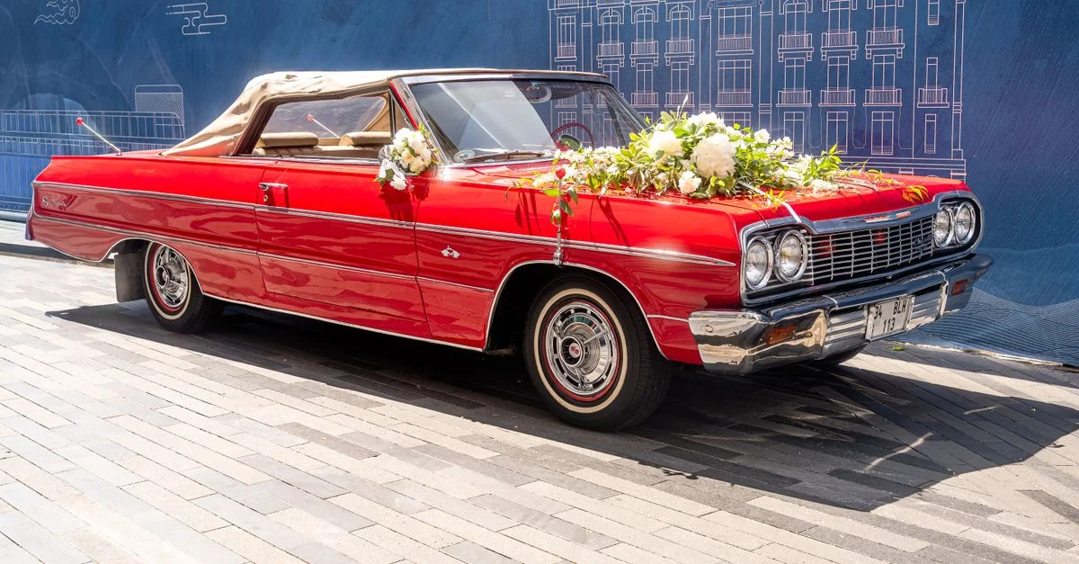 Une voiture décapotable rouge vintage, ornée de fleurs blanches fraîches et de feuillage vert, est garée dans une rue de la ville.