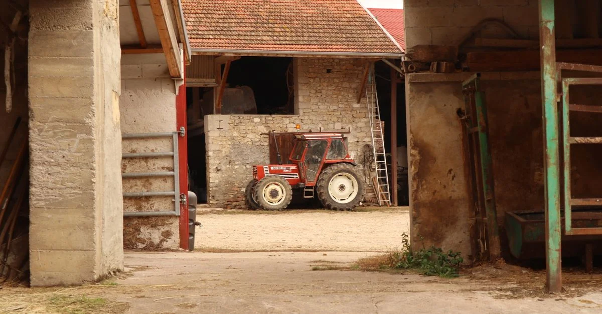 Un tracteur vintage garé à l'intérieur d'une grange dans un cadre de ferme rustique.