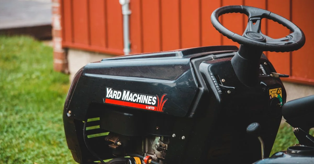 Vue détaillée d'une tondeuse autoportée Yard Machines garée sur une pelouse verte à côté d'un abri rouge.