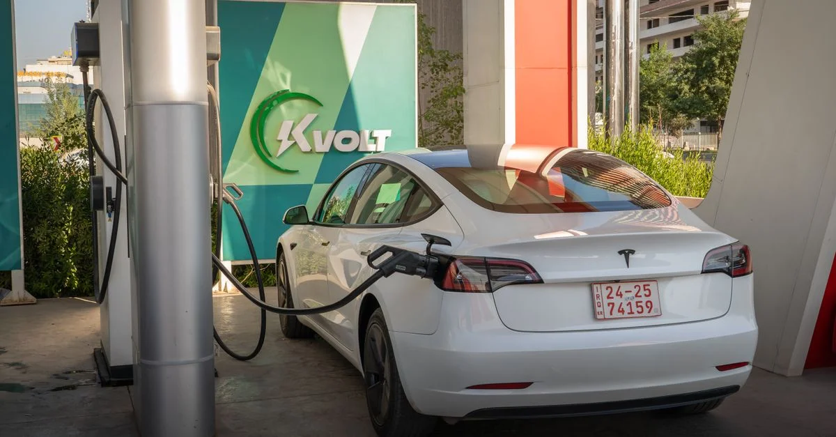 Une Tesla Model 3 blanche en charge à une station de véhicule électrique extérieure avec le branding Kvolt.