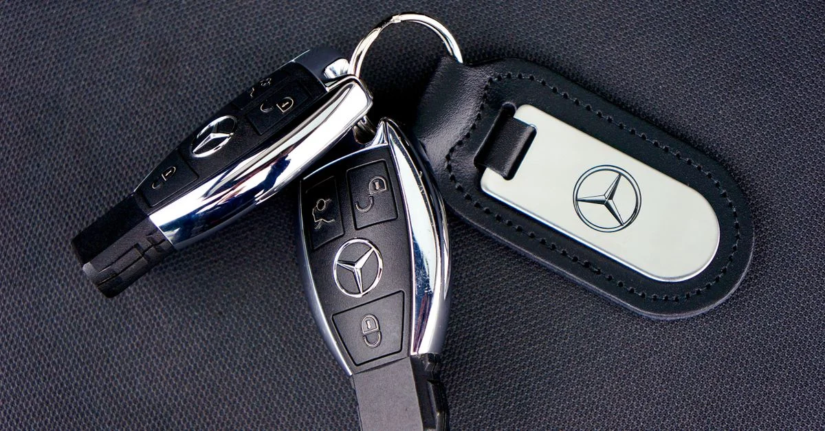 Gros plan sur des clés de voiture Mercedes-Benz avec un porte-clés en cuir sur un fond de tissu sombre.