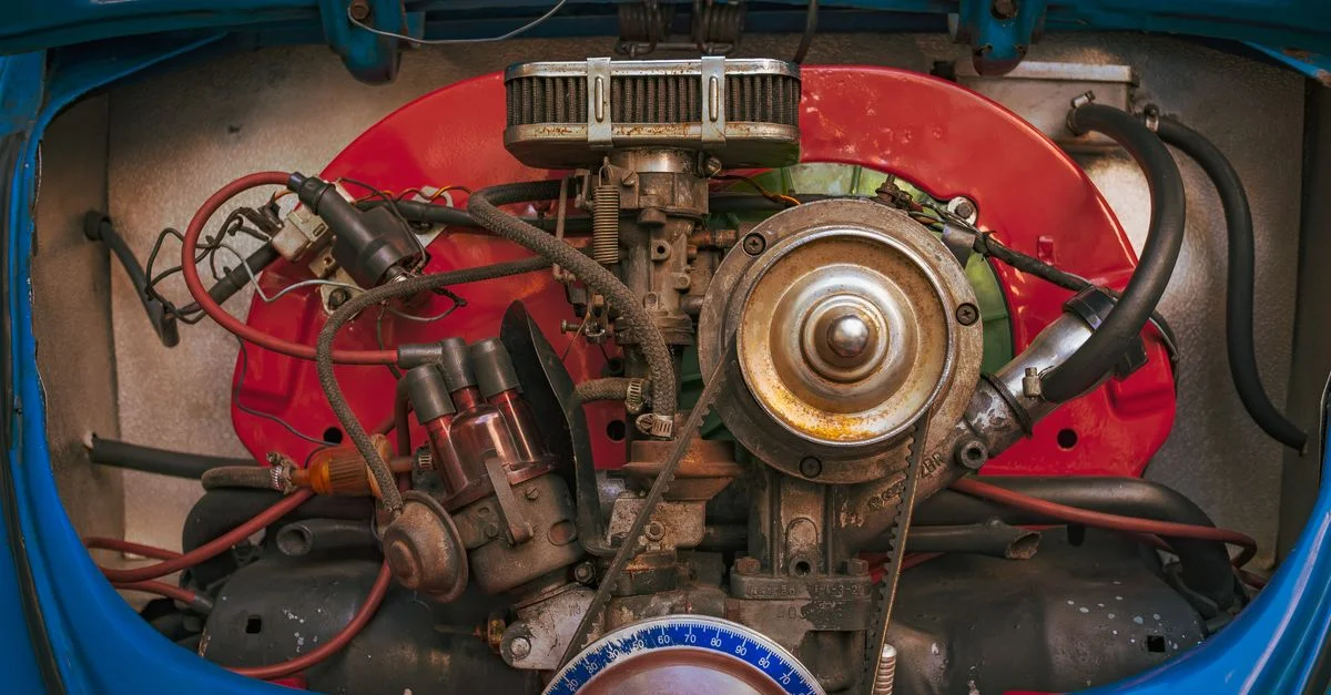Vue détaillée d'un moteur de voiture ancienne, mettant en valeur ses composants mécaniques et son boîtier coloré.