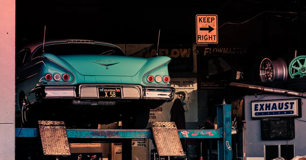 Voiture classique turquoise vintage sur un élévateur de garage, mettant en valeur son charme rétro.