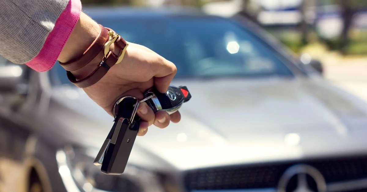 Une image en gros plan d'une main tenant des clés de voiture devant un arrière-plan de voiture de luxe, en extérieur.