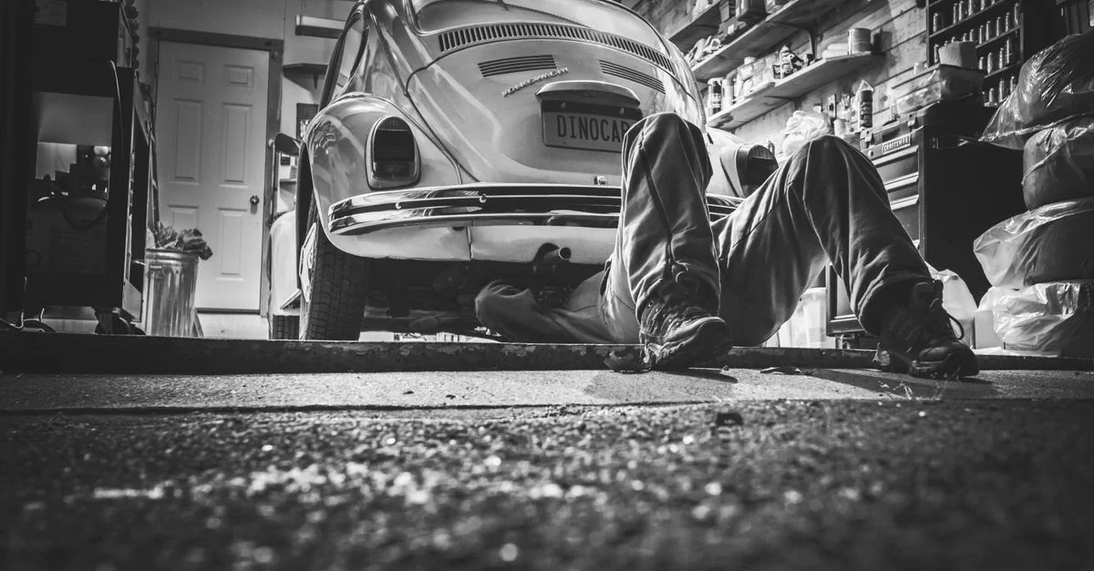 Mécanicien travaillant sous une Volkswagen Coccinelle classique dans un garage vintage.