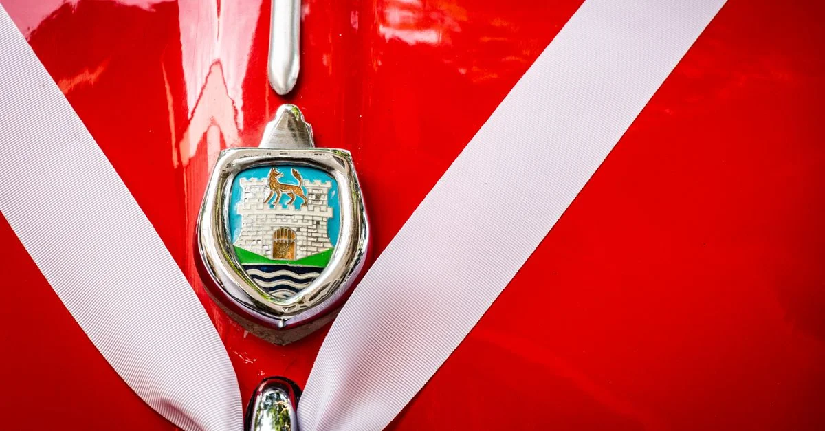Vue détaillée d'un emblème de voiture ancienne sur un véhicule rouge orné d'un ruban blanc.