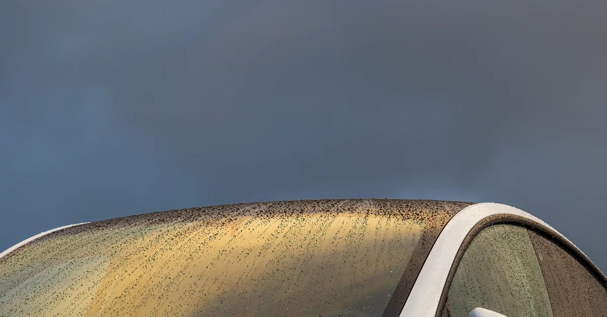 Une vue détaillée du pare-brise d'une voiture recouvert de gouttes de pluie avec un ciel sombre et dramatique.