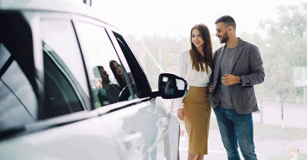 Un couple souriant examine une nouvelle voiture chez un concessionnaire, enthousiaste à l'idée de son achat.