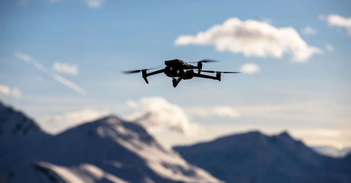 Un drone vole au-dessus de sommets pittoresques recouverts de neige sous un ciel bleu clair, capturant des paysages à couper le souffle.