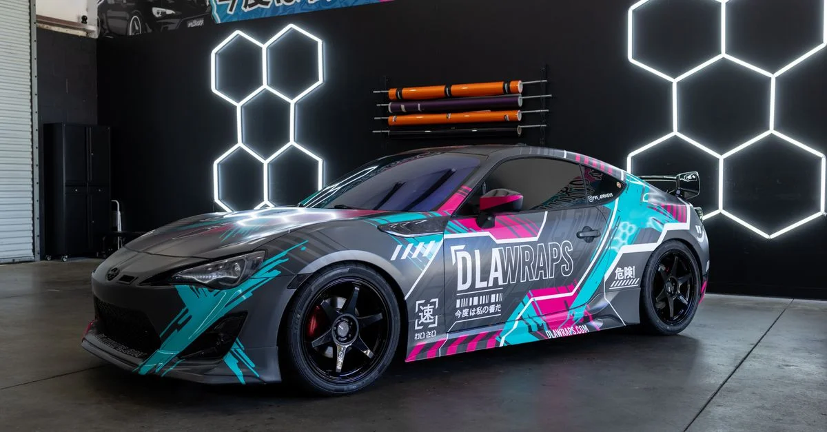 Photo dynamique d'une voiture de sport élégante avec un vinyle personnalisé coloré par DLA Wraps dans un cadre d'atelier.