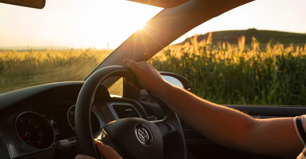 Vue du conducteur sur une route de campagne au coucher du soleil, mettant l'accent sur le volant.
