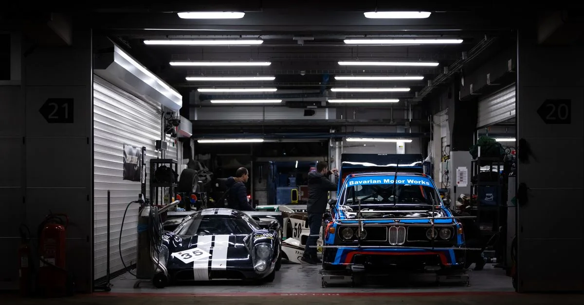 Des BMW classiques et des voitures de course dans un garage de nuit, illustrant la passion pour l'automobile.