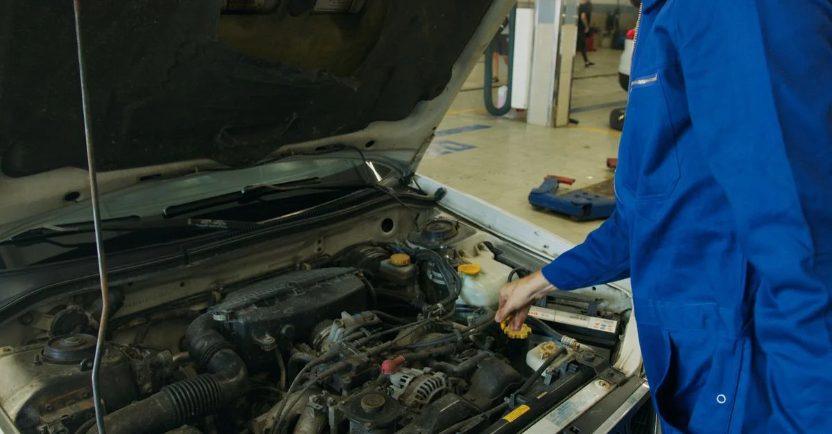 Mécanicien en combinaison bleue inspectant un moteur de voiture ouvert dans un atelier automobile.
