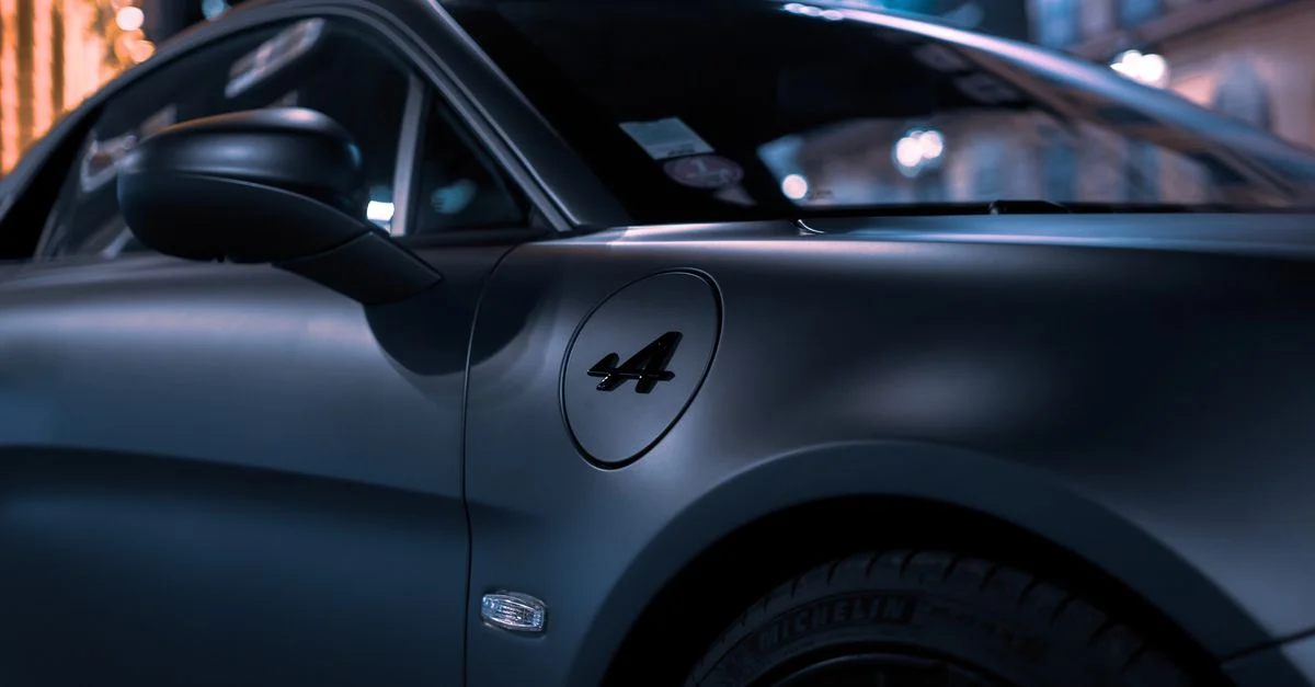 Gros plan d'une voiture de sport Alpine A110 de luxe avec finition mate sous les lumières de la ville la nuit.