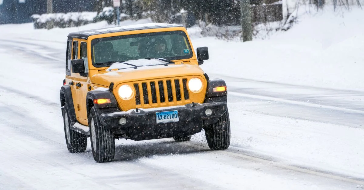 Un SUV jaune vif se faufile dans une rue urbaine enneigée en conditions hivernales.