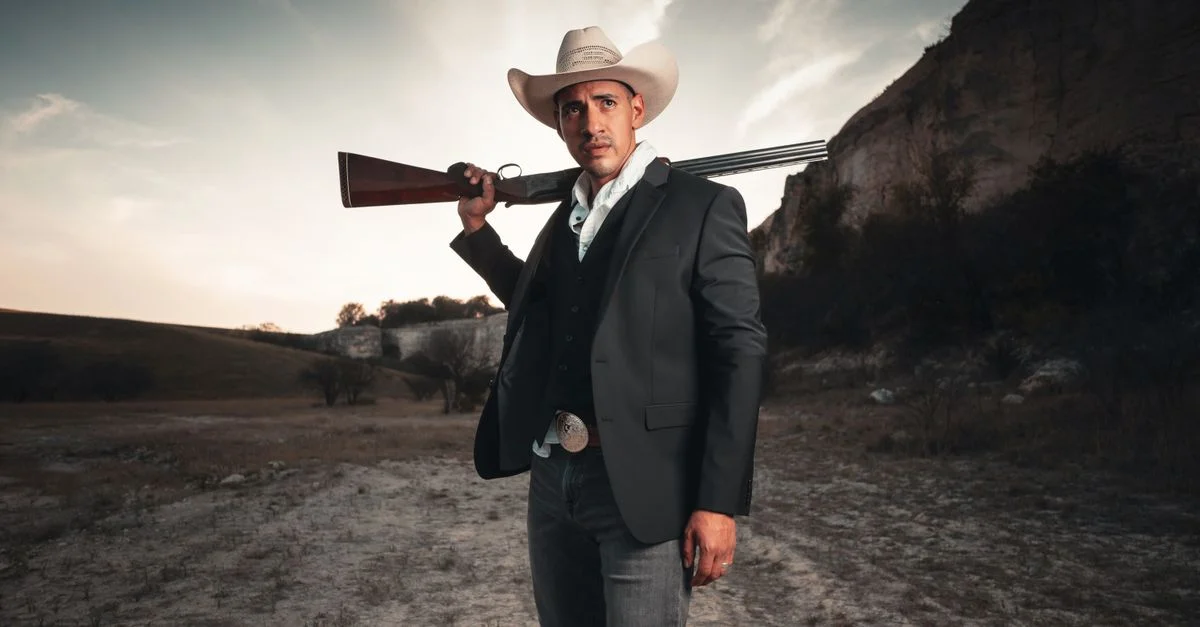 Portrait d'un cowboy en costume avec un fusil de chasse contre un paysage texan rude.