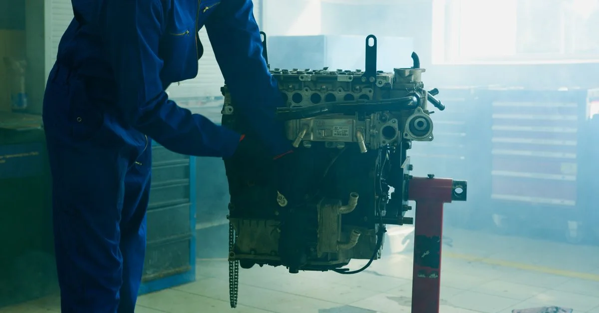 Mécanicien en bleu de travail inspectant un moteur dans un garage intérieur.
