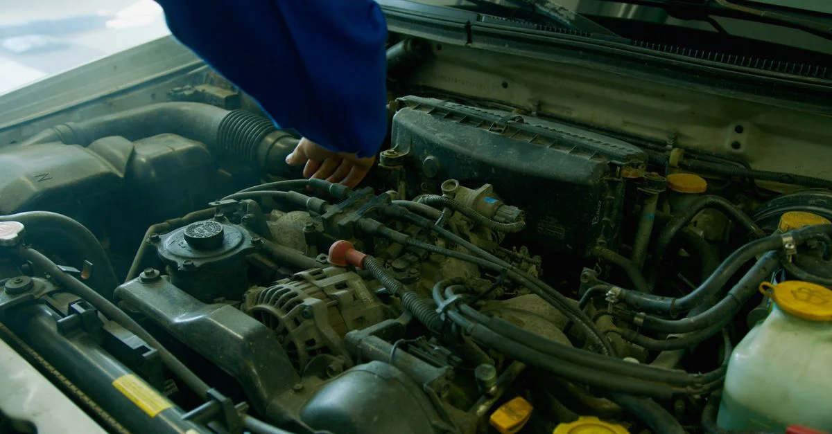 Mécanicien en uniforme bleu travaillant sur un moteur de voiture dans un environnement de garage.
