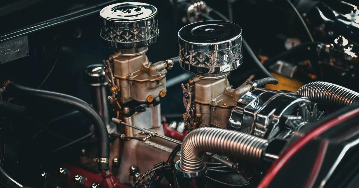 Gros plan d'un moteur de voiture classique présentant des détails complexes de carburateurs jumeaux et de composants métalliques.