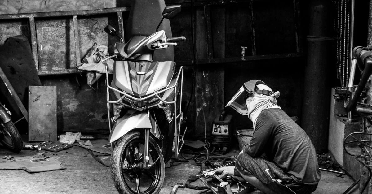 Soudeur réparant une moto dans un atelier, capturée en noir et blanc.
