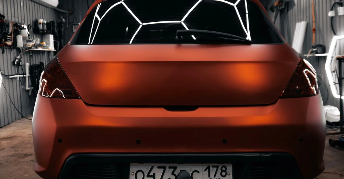Une élégante voiture orange dans un garage, un éclairage vif mettant en valeur ses lignes fluides.