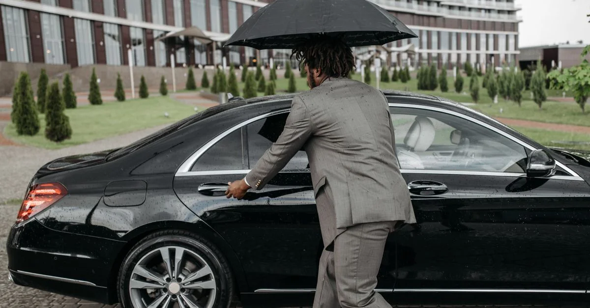 Un homme en costume ouvrant la porte d'une voiture tout en tenant un parapluie sous la pluie.