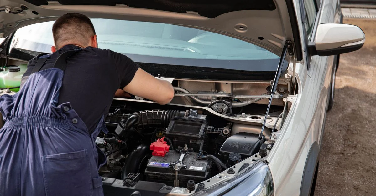 Un mécanicien répare un moteur de voiture en plein air, se concentrant sur l'entretien du véhicule.