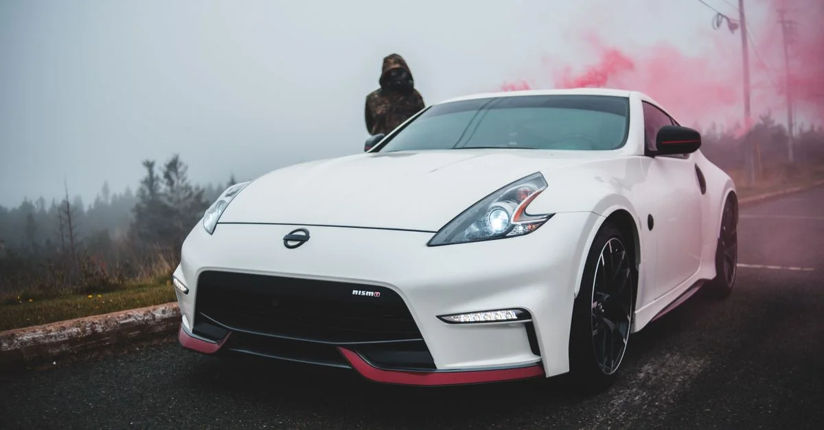 Une voiture de sport blanche élégante garée sur une route brumeuse avec de la fumée rose en arrière-plan, transmettant un sentiment de mystère.
