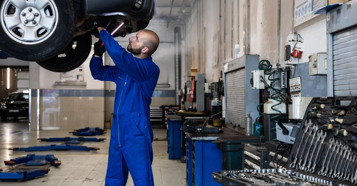 Mécanicien inspectant une voiture surélevée dans un atelier automobile pour des services d'entretien et de réparation.