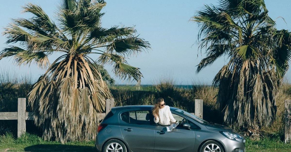 Jeune femme dans une voiture près des palmiers sur une route côtière pittoresque, incarnant l'aventure et l'exploration.