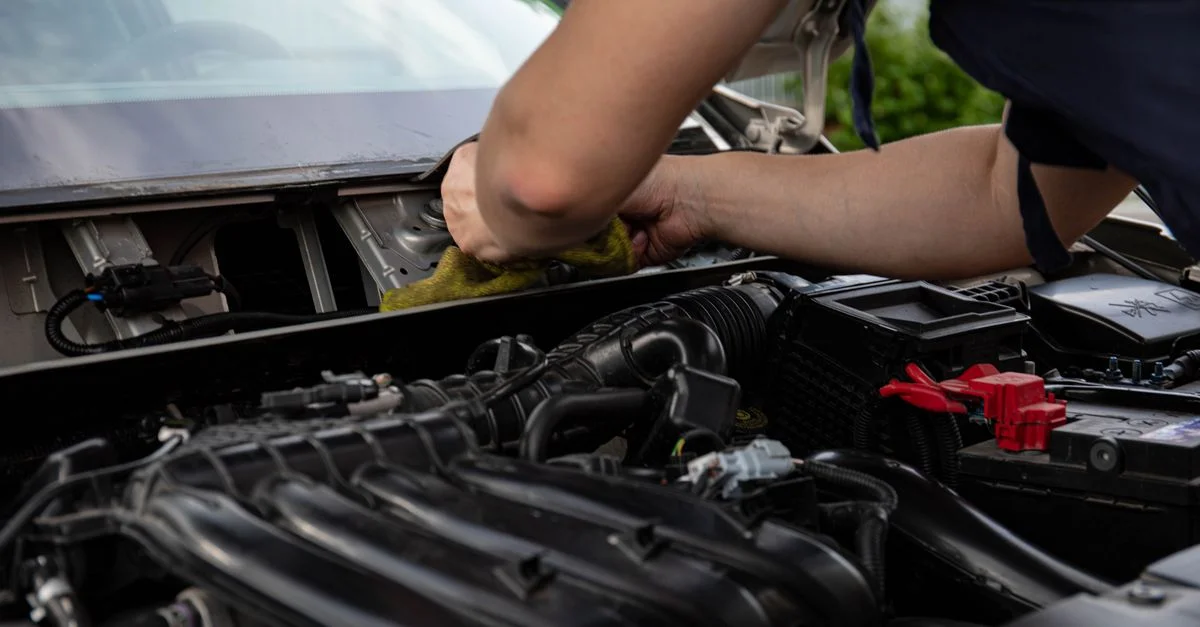 Gros plan d'un mécanicien travaillant sur un moteur de voiture, mettant en valeur les mains et les détails du moteur.