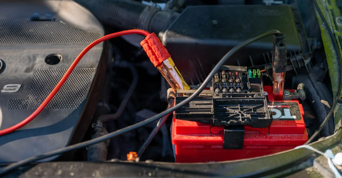 Gros plan d'une batterie de voiture avec des câbles de démarrage attachés dans un compartiment moteur.