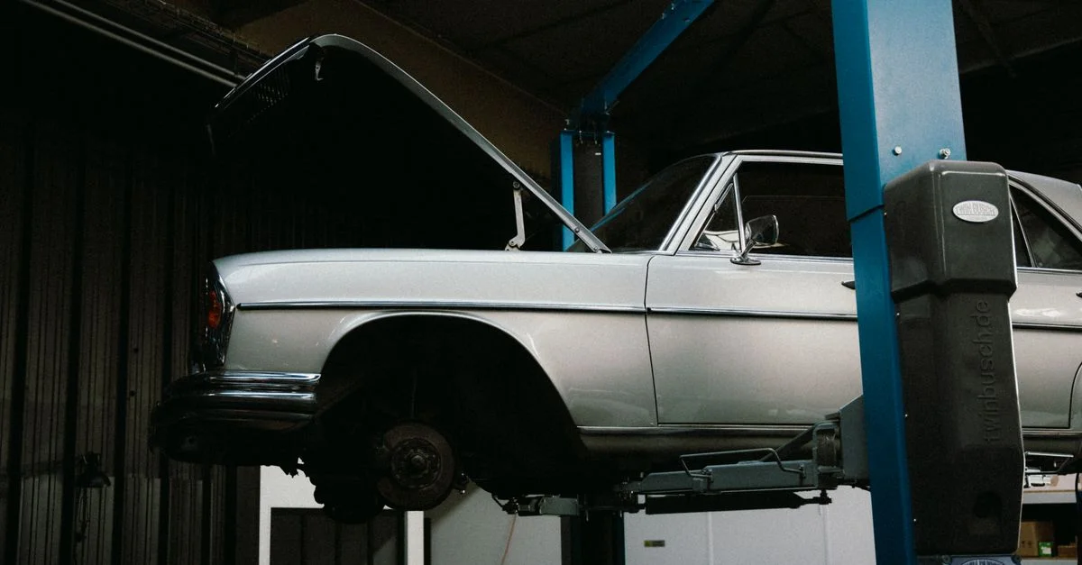 Une voiture ancienne en réparation sur un élévateur hydraulique à l'intérieur d'un atelier de réparation automobile.