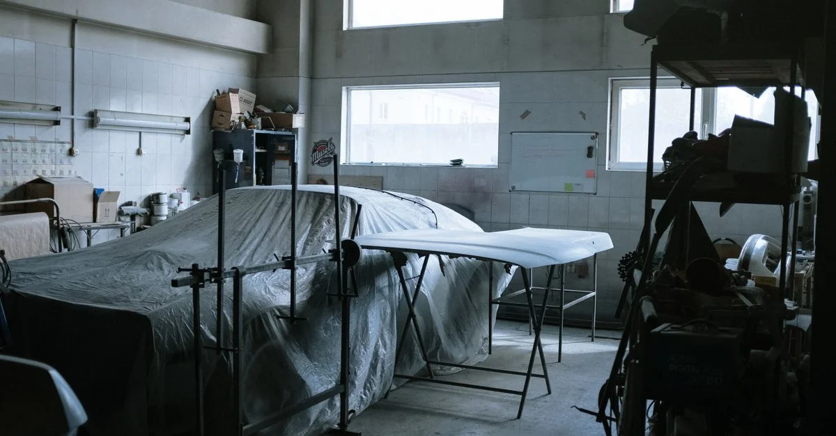Un atelier de réparation automobile intérieur avec une voiture couverte, des outils et de l'équipement visibles.