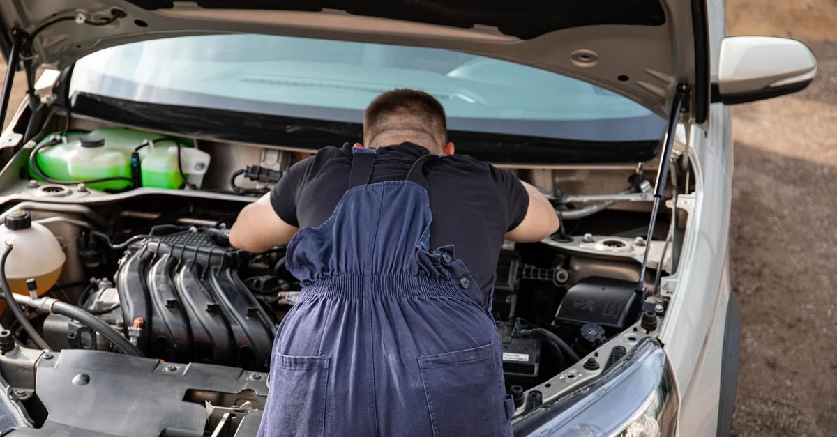 Mécanicien en salopette travaillant sur un moteur de voiture en extérieur, offrant des services de réparation de véhicules.