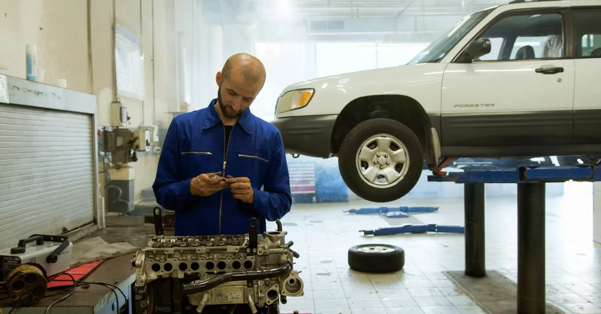 Un mécanicien en uniforme bleu inspecte un moteur dans un atelier de réparation automobile professionnel.