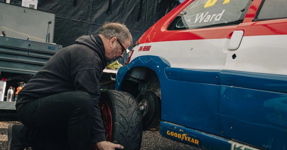 Un mécanicien change un pneu sur une voiture de course bleue et rouge lors d'un arrêt aux stands.