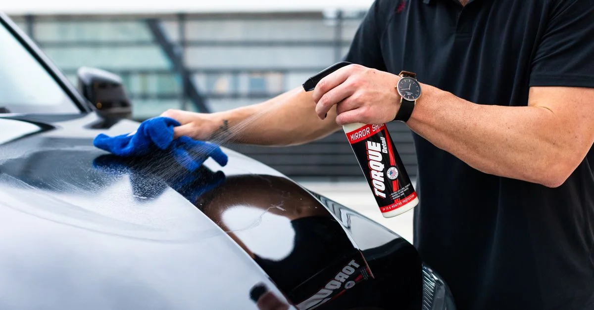 Un homme nettoyant le capot d'une voiture noire avec un spray et un chiffon en microfibre.