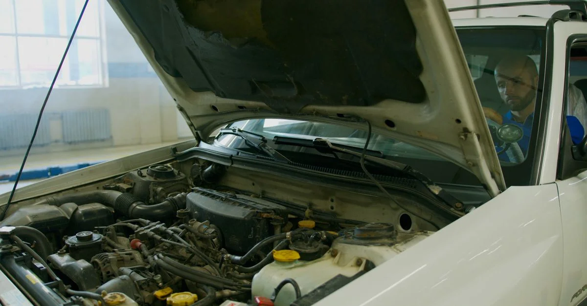 Mécanicien vérifiant le moteur de la voiture sous le capot ouvert dans un garage.