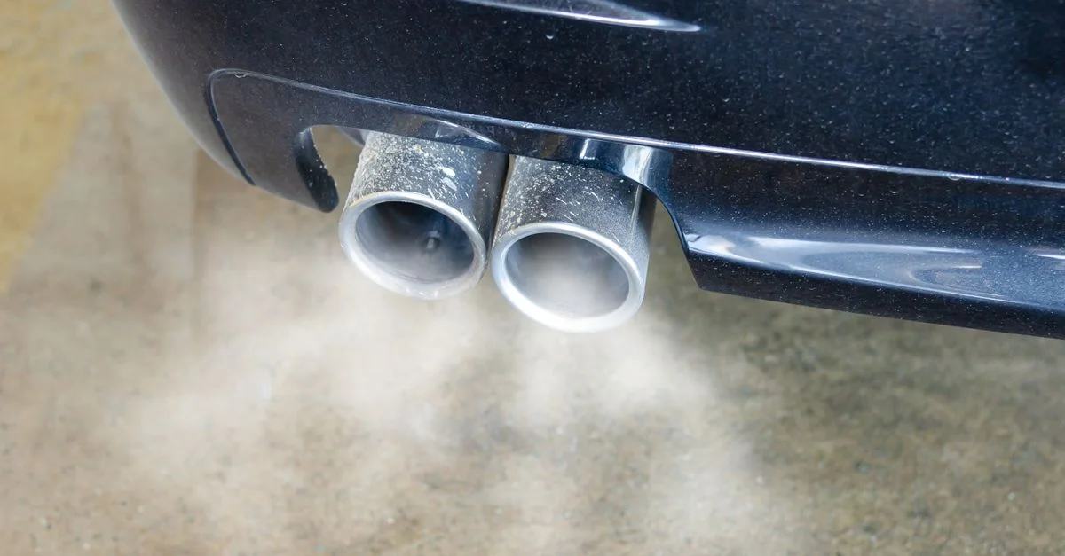 Gros plan sur les tuyaux d'échappement d'une voiture émettant de la fumée visible, mettant en avant la pollution de l'air.