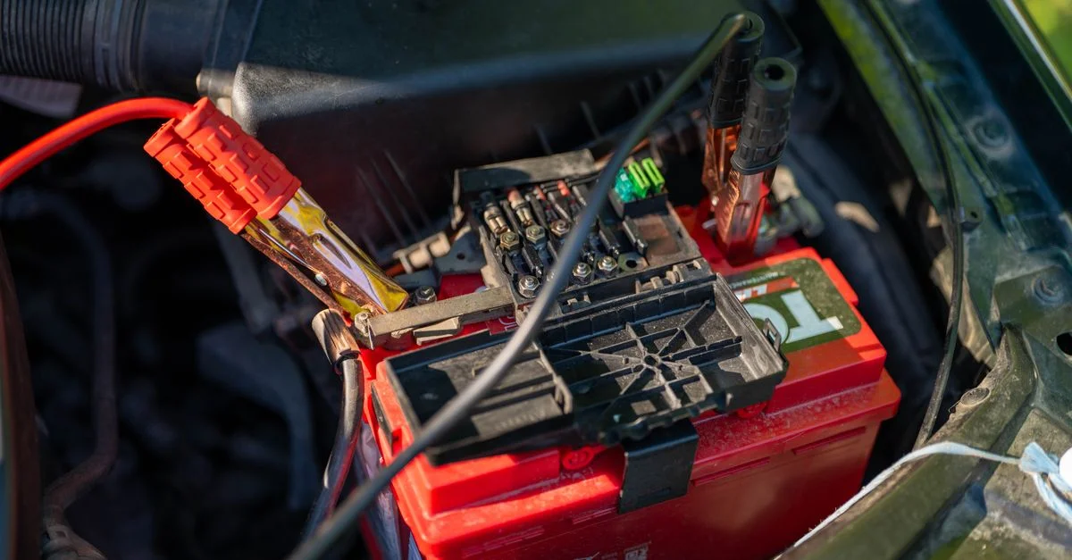 Vue rapprochée d'une batterie de voiture avec des câbles de démarrage rouges connectés, en extérieur.