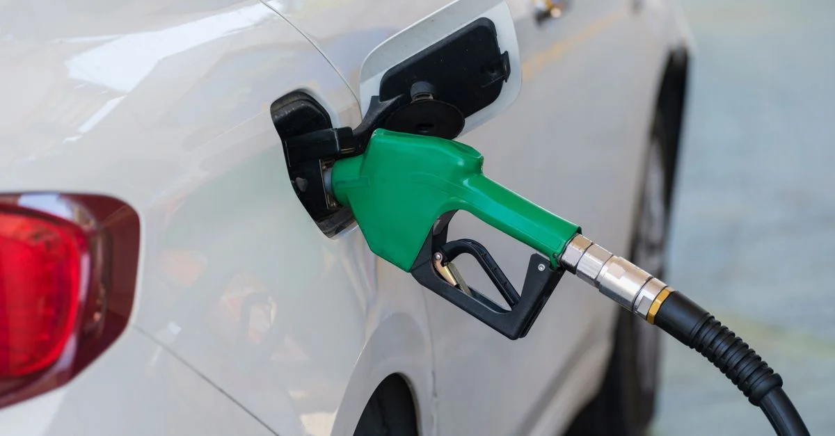 Gros plan d'un pistolet vert faisant le plein d'une voiture blanche à une station-service.