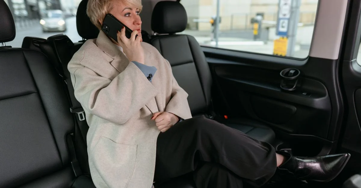 Femme dans une voiture en train de passer un appel téléphonique, portant un manteau et se reposant confortablement.