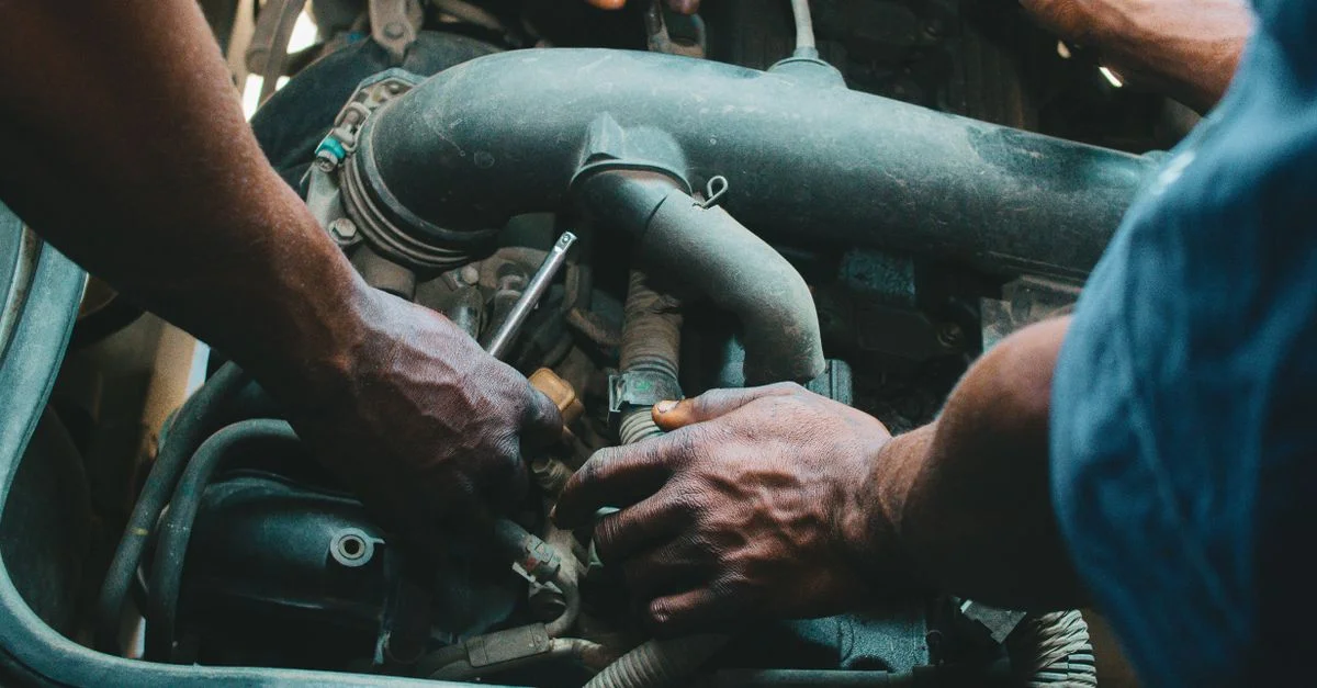 Gros plan sur des mécaniciens travaillant sur un moteur de véhicule, illustrant le travail d'équipe et la précision dans l'entretien automobile.