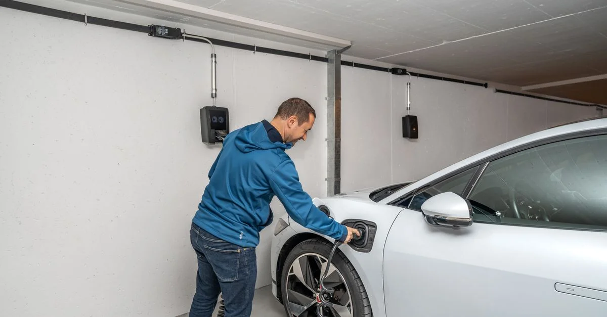 Un homme branche une voiture électrique à une borne de recharge dans un garage intérieur moderne.